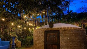 Una estructura de piedra circular con una puerta de madera oscura, rodeada de vegetación y luces de cuerda.