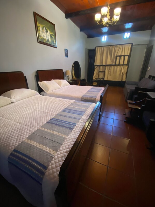 A hotel room with two beds, a wooden ceiling, a chandelier, a painting, and a view of the outside. - Ruaj Hostal (Antigua Guatemala)