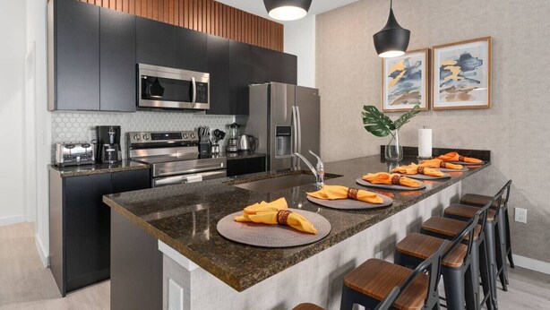 Une cuisine moderne avec des meubles de couleur sombre, des appareils en acier inoxydable et un îlot central doté de tabourets de bar.