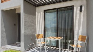 Une terrasse avec deux chaises et une table, une porte-fenêtre coulissante et un petit espace extérieur avec une porte et des marches.