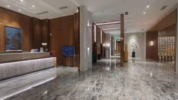 A hotel lobby with a reception desk, marble flooring, and a modern interior design.