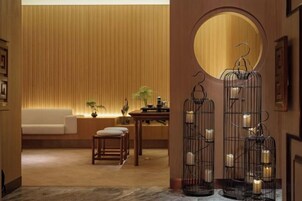 Una habitación cálidamente iluminada con un sofá, una mesa con una lámpara y una jaula decorativa con velas.