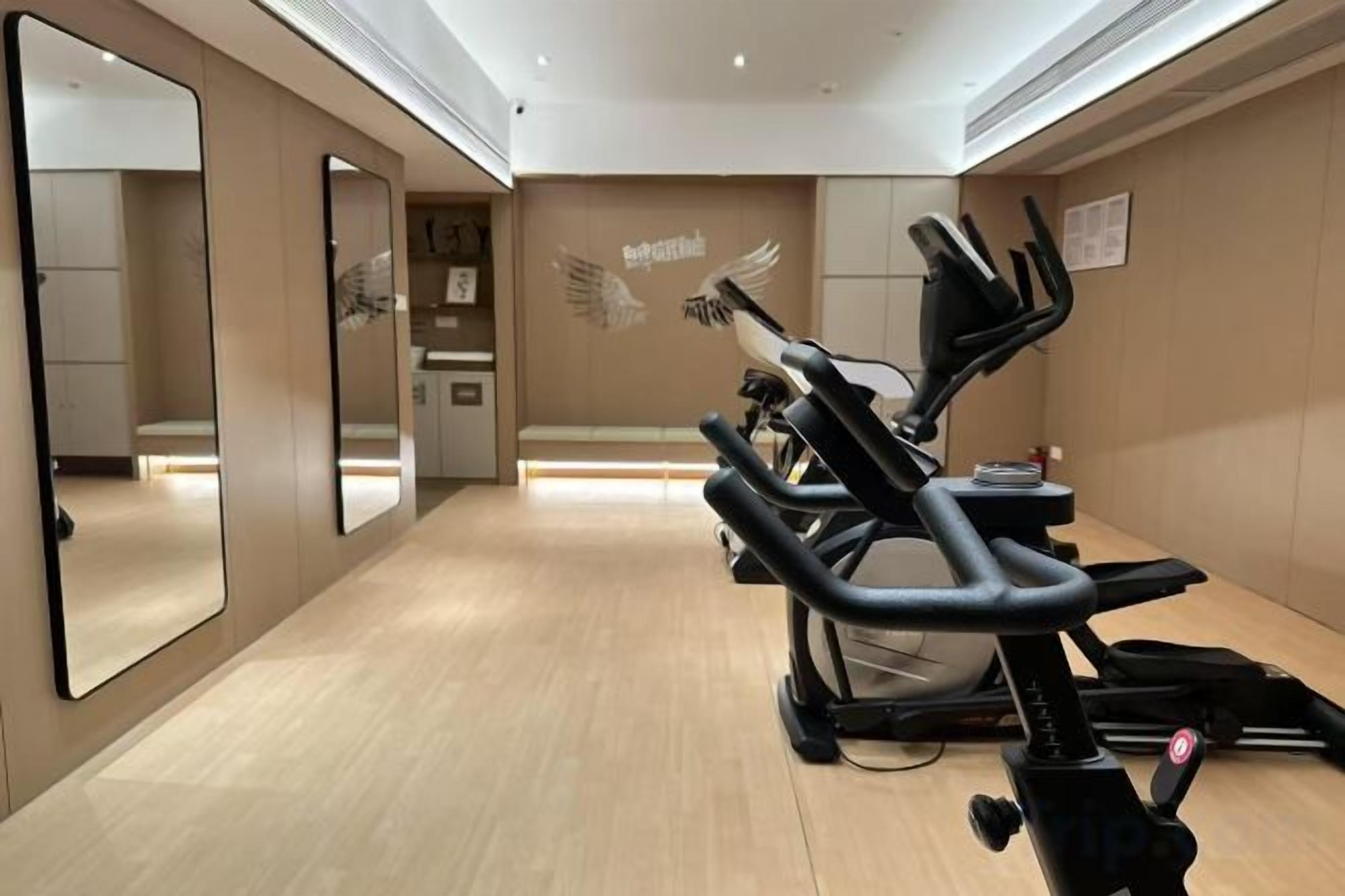 Une salle de sport équipée de matériel d’exercice, dotée d’un grand miroir et d’un mur orné d’un motif représentant des ailes.