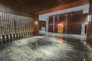 Un vestíbulo con piso de mármol pulido, paneles de madera y una zona de recepción con pantalla digital.