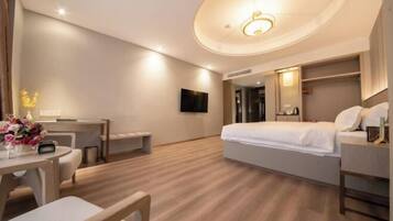 A hotel room with a bed, a desk, a chair, a TV, and a small table with flowers.