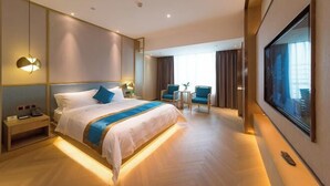 Une chambre d’hôtel moderne, dotée d’un grand lit, de tables de chevet, d’un bureau, de chaises et d’une grande fenêtre.