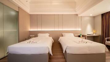 A hotel room with two single beds, a small bedside table, a nightstand, and a chair.