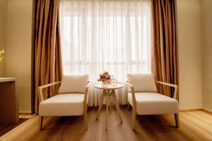 Una habitación con dos sillones blancos frente a una pequeña mesa redonda con un florero.