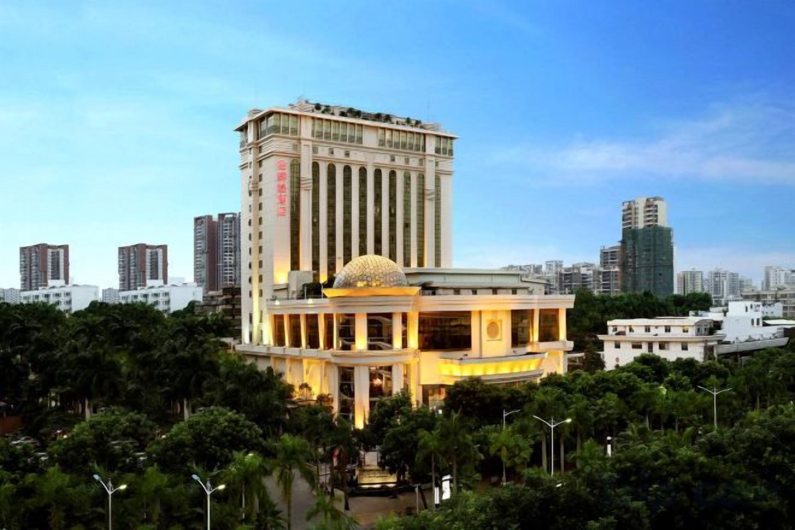 A hotel with a prominent dome structure, a tall building in the background, and a well-maintained garden area.