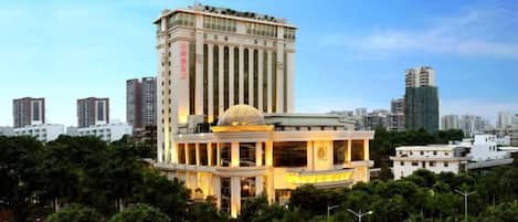 A hotel with a prominent dome structure, a tall building in the background, and a well-maintained garden area.