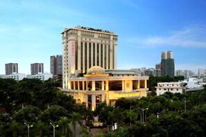 A hotel with a prominent dome structure, a tall building in the background, and a well-maintained garden area. - Golden Splendid Hotel (Zhanjiang)