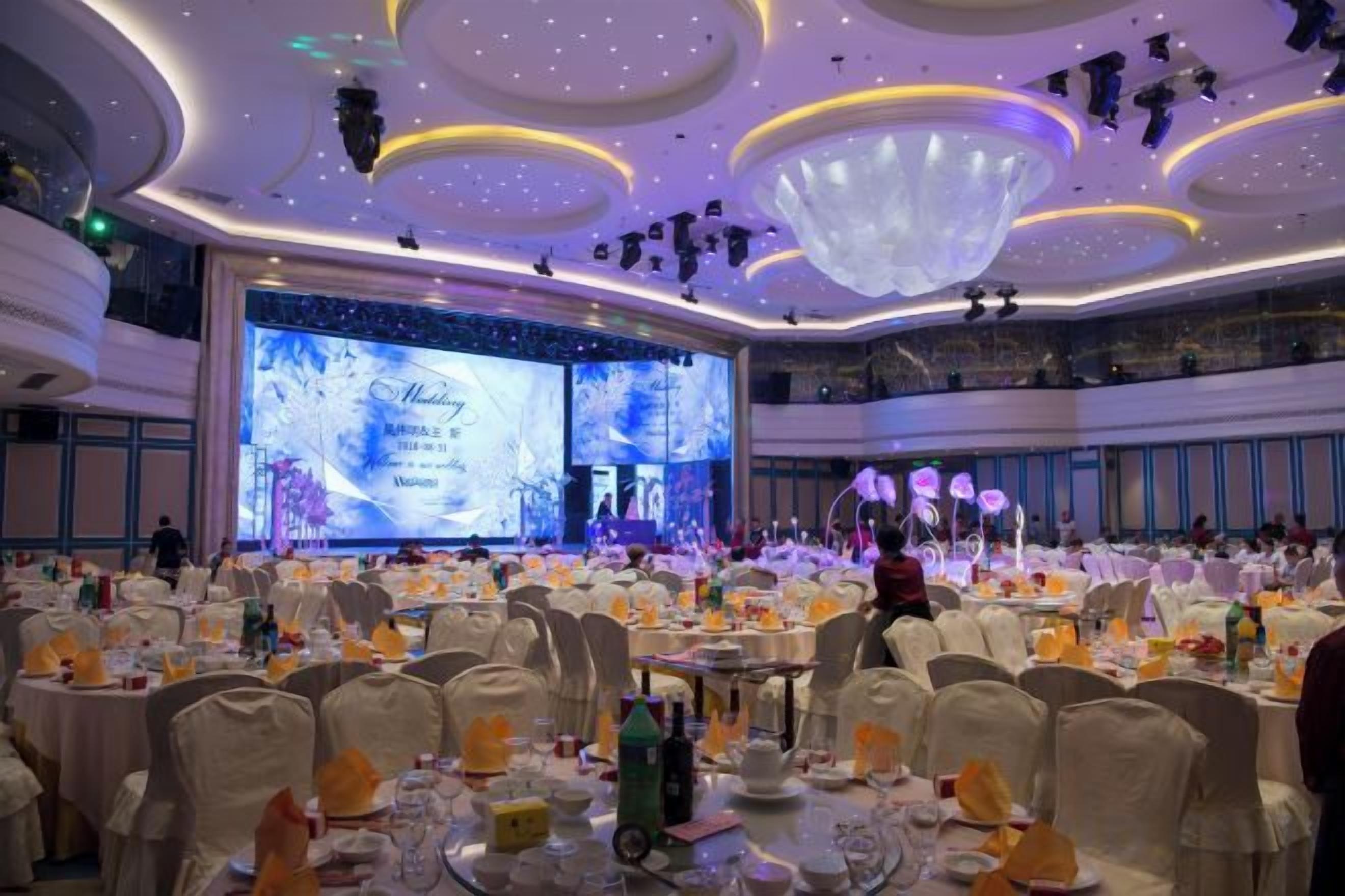 A banquet hall with round tables, chairs, and a stage for presentations.