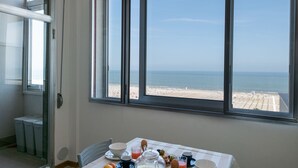 Ein Frühstückstisch mit Blick auf Strand und Meer durch große Fenster.