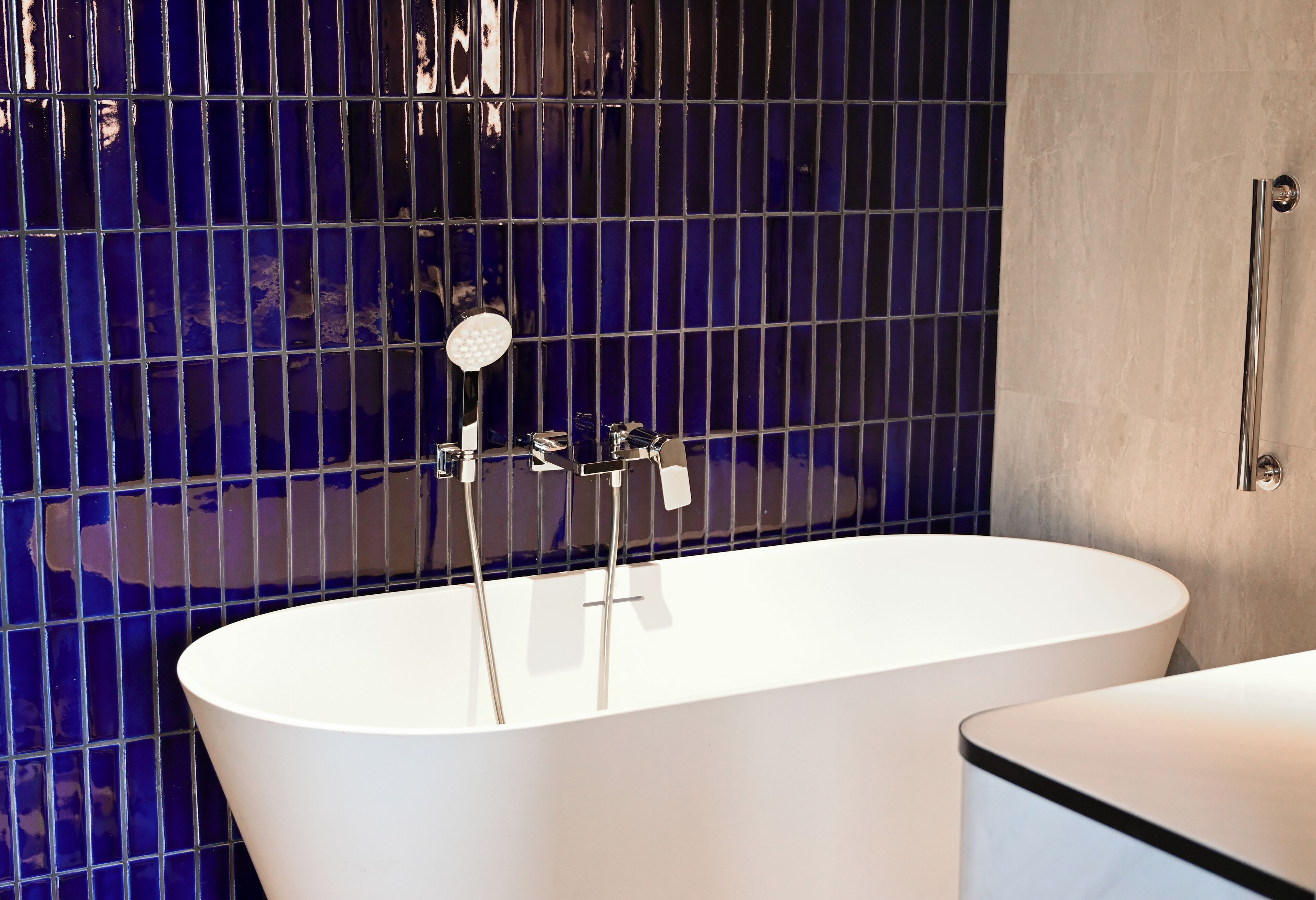 A modern bathroom with a freestanding bathtub, a white sink, and a blue-tiled wall.