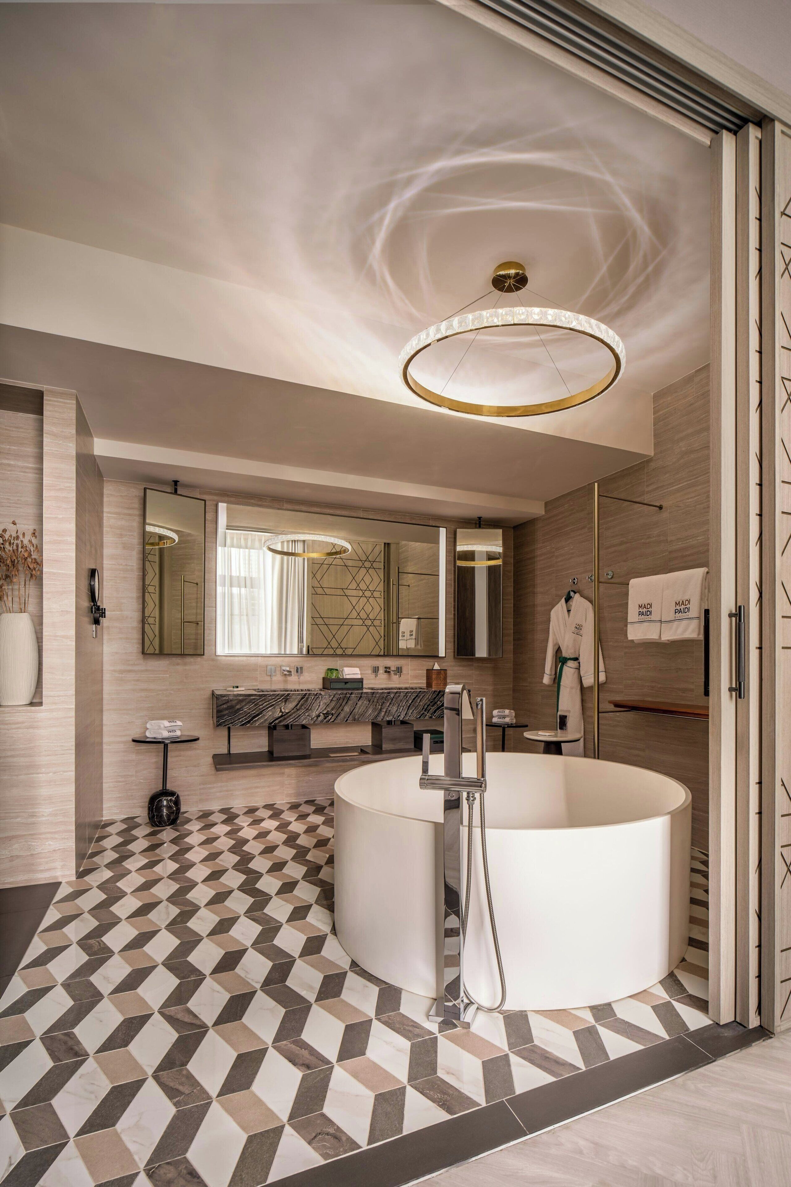 Un baño moderno con una bañera independiente, un espejo grande y un piso con diseño geométrico.