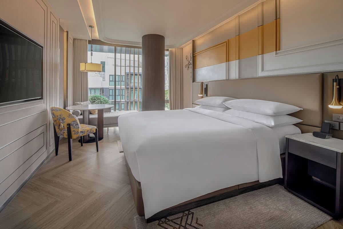 A modern hotel room with a large bed, a small table with a chair, a large window, and a view of the city.