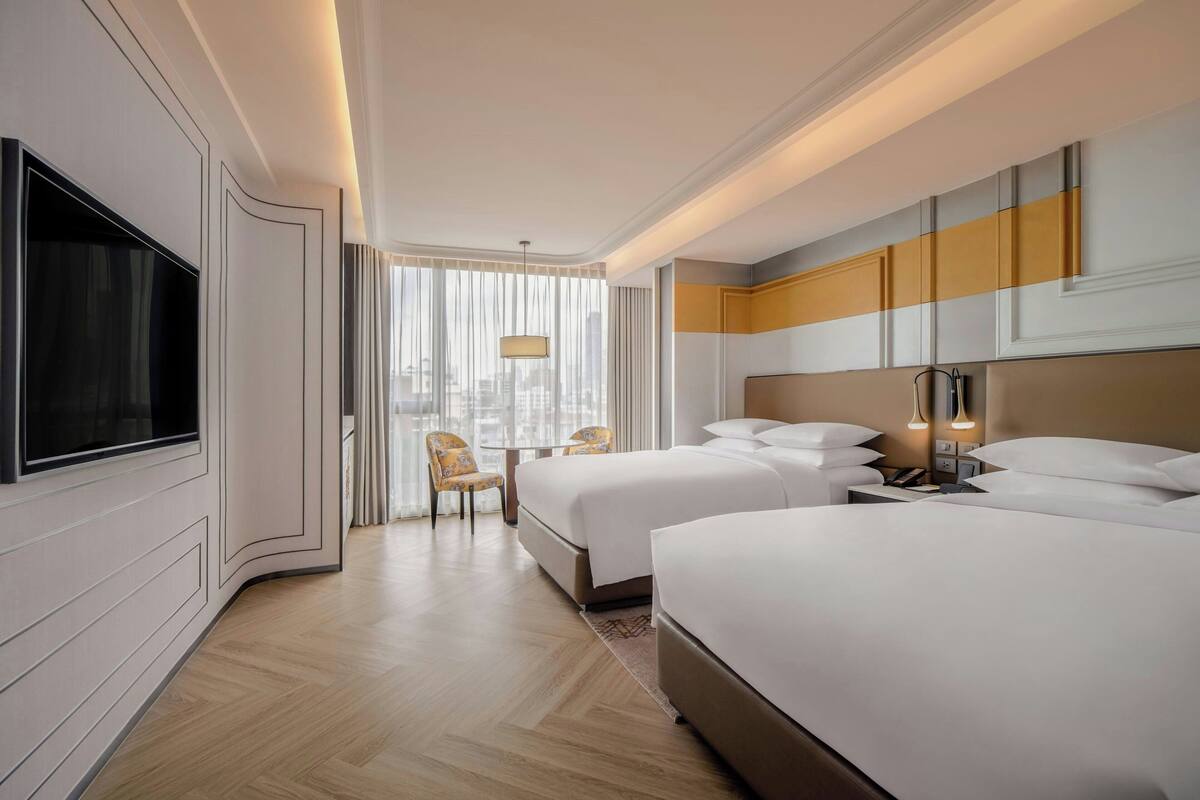 A hotel room with two beds, a TV, a desk, and a chair.