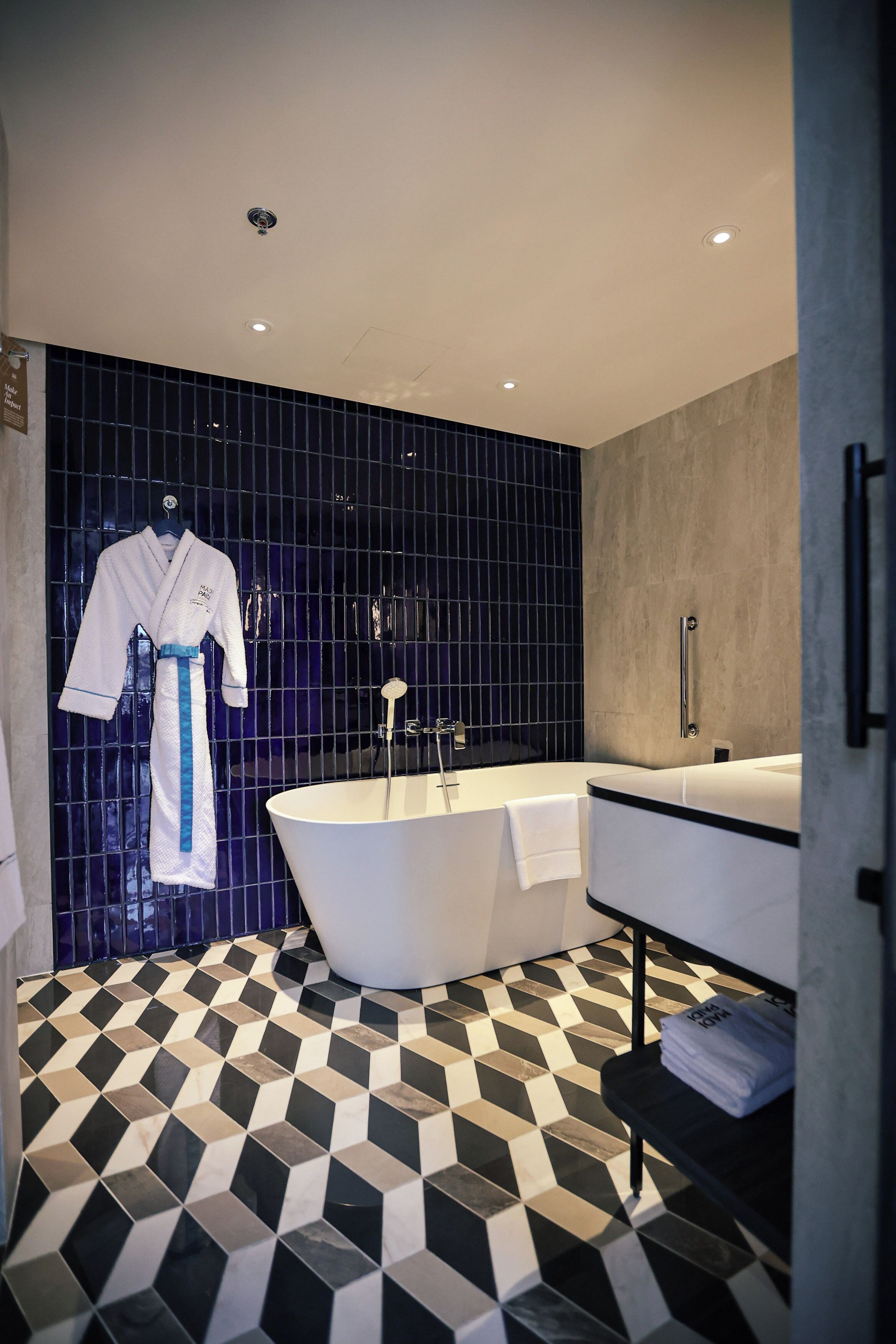 A modern bathroom with a black and white checkered floor, a white bathtub, and a large mirror.