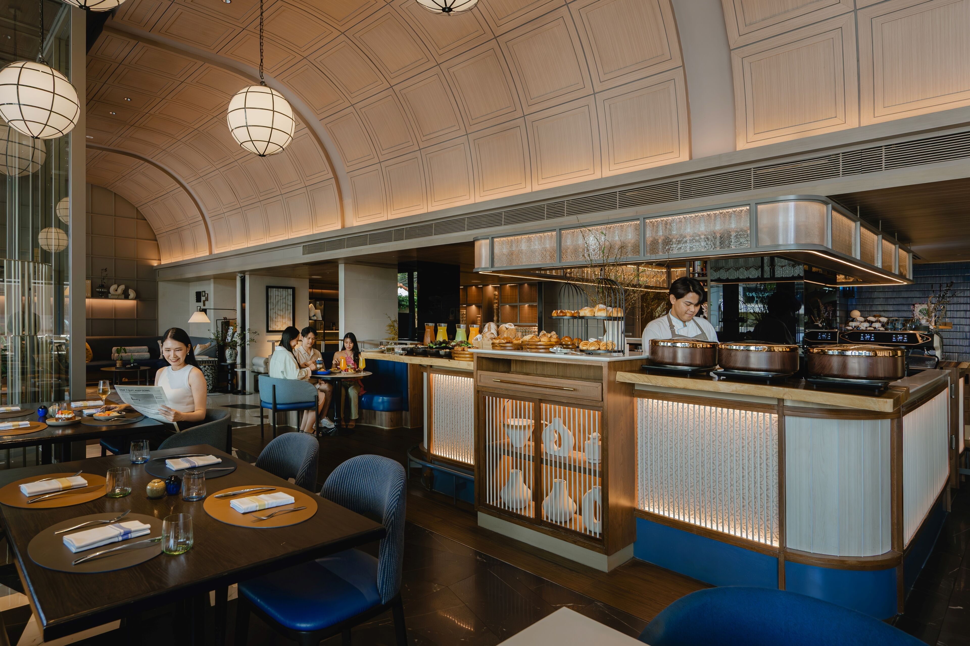 Een restaurant met een gebogen plafond, een bar met een kok, en tafels met tafelonderleggers.