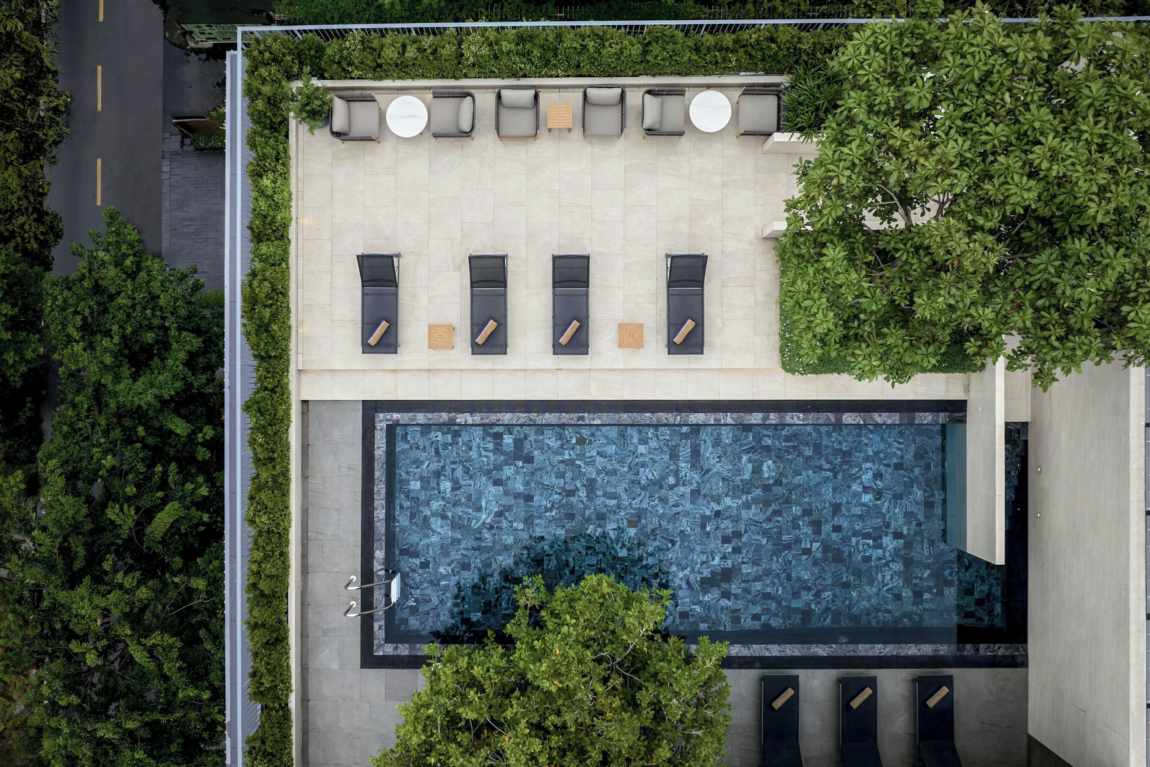 Vue aérienne d’un bâtiment moderne doté d’un espace de détente sur le toit, d’une piscine et d’un espace vert environnant.