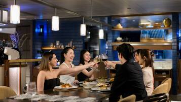 A group of people toasting at a dinner table in a modern restaurant with pendant lighting and a blue-lit interior.