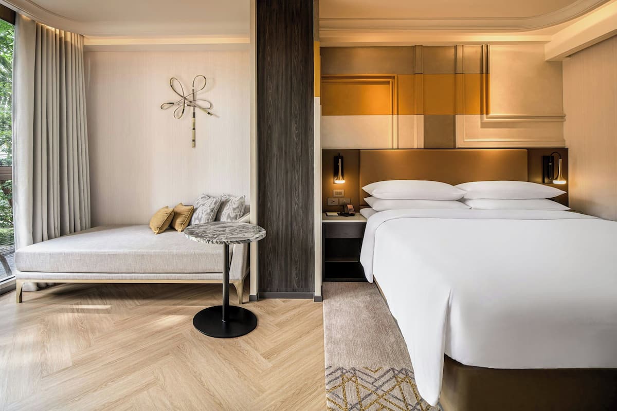A modern hotel room with a sofa, a small table, a bed, and a nightstand.