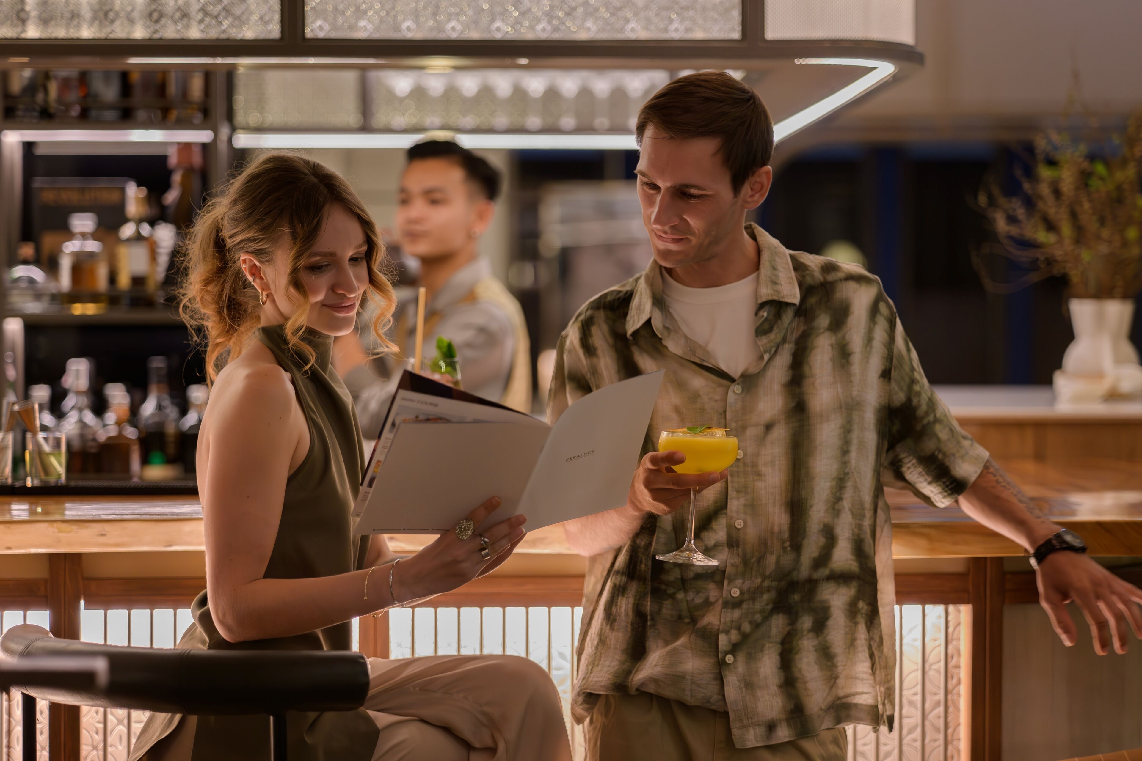 Una zona de bar con mostrador, carta y una persona sosteniendo una bebida.