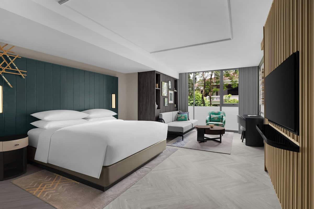 A modern hotel room with a large bed, a sofa, a TV, and a view of the outdoors.