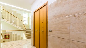 A hallway with a wooden double door, a staircase with a glass railing, and a tiled floor. - La Dimora dell'Avvocato (Naples)