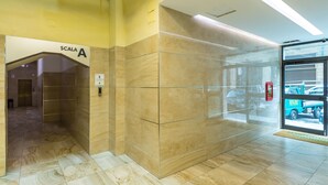 A modern elevator interior with a marble floor and walls, a visible emergency phone, and a door leading to a hallway with a vehicle outside. - La Dimora dell'Avvocato (Naples)