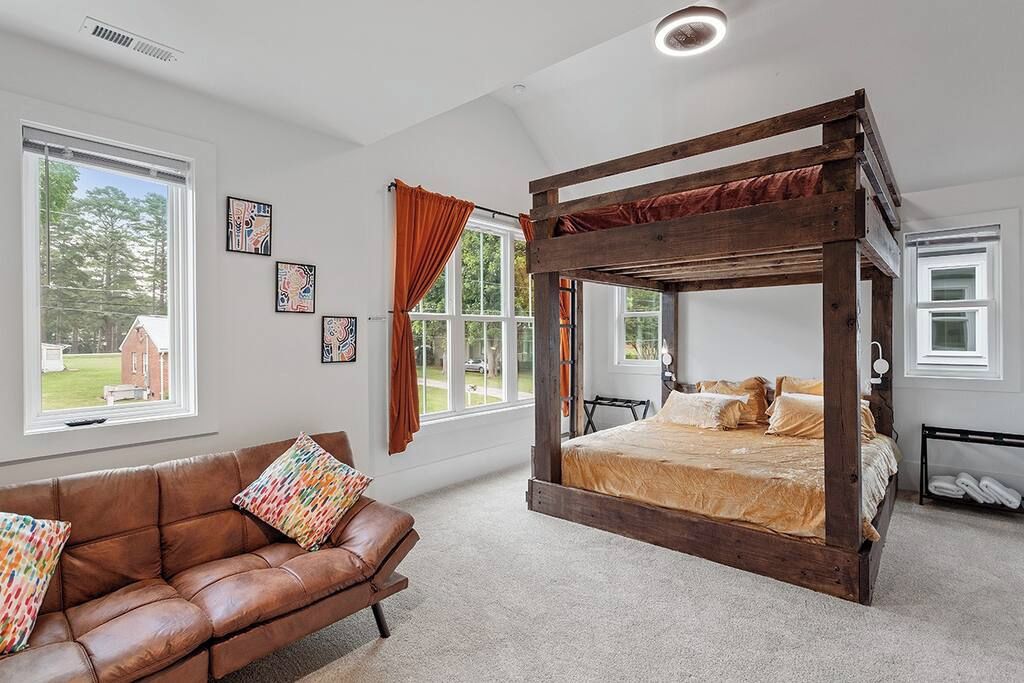A bedroom with a four-poster bed, a leather sofa, and large windows.