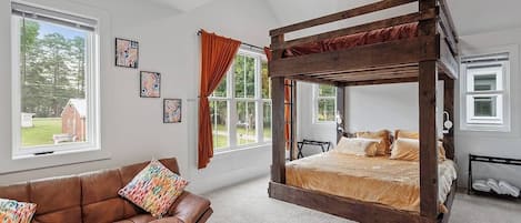 A bedroom with a four-poster bed, a leather sofa, and large windows.