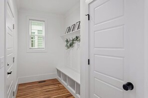 A hallway with white walls, a wooden floor, a window with blinds, and a door with a black handle.