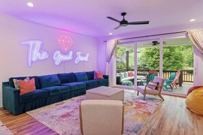 Una sala de estar con un sofá azul, un letrero de neón que dice 'The Grand Jewel' y vistas a una terraza exterior a través de un ventanal.