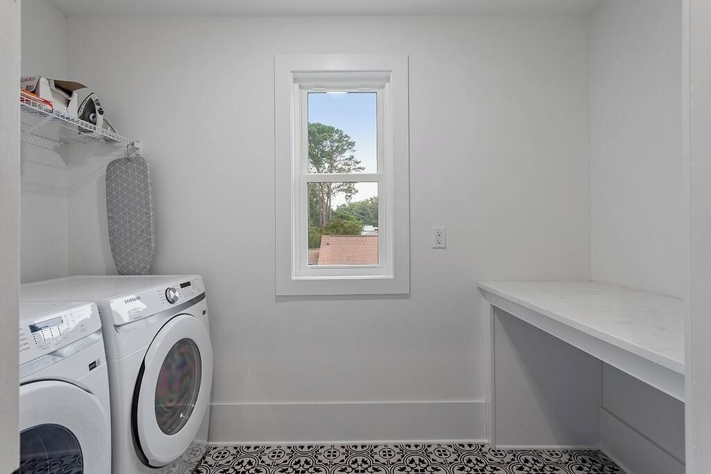A laundry room with a washing machine, a dryer, a window, and a white shelf.