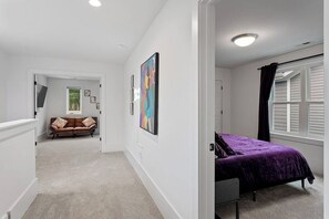 Un dormitorio con cama, una ventana con cortinas y un pasillo que conduce a otra habitación.