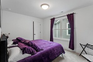 Un dormitorio con cama, ventana con cortinas, una puerta y una lámpara en el techo.