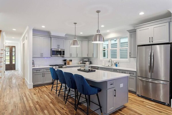 A modern kitchen with a central island, bar stools, stainless steel appliances, and pendant lighting.