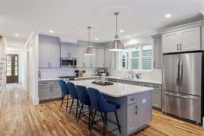 A modern kitchen with a central island, bar stools, stainless steel appliances, and pendant lighting.