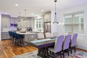 A modern kitchen with a central island, bar stools, pendant lighting, and a dining area with chairs.