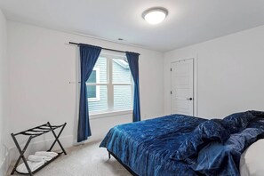 A bedroom with a bed, a drying rack, a window with curtains, and a door.