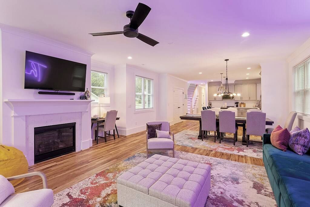 A spacious living room with a fireplace, a television mounted on the wall, and a dining area with chairs and a table.