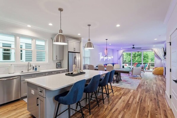 A modern kitchen with a central island, bar stools, pendant lighting, and a view to a deck area.