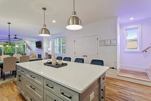 Una cocina moderna con una isla grande, luces colgantes y un comedor con sillas.