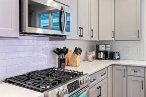 A modern kitchen with white cabinets, a stainless steel range, and a microwave.