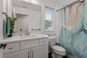 Un baño moderno con tocador blanco, inodoro y cortina de ducha con diseño abstracto.