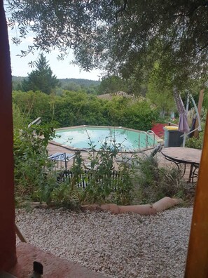 Una piscina rodeada de vegetación, con un patio y vistas a las colinas al fondo.