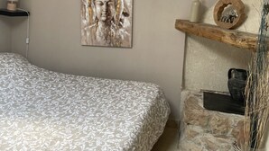 A bedroom with a bed, a wall-mounted painting, a shelf with decorative items, and a fireplace. - Maison "La Miloune" au Coeur de la Provence Verte, Dans Quartier Calme et Arboré (Le Val)