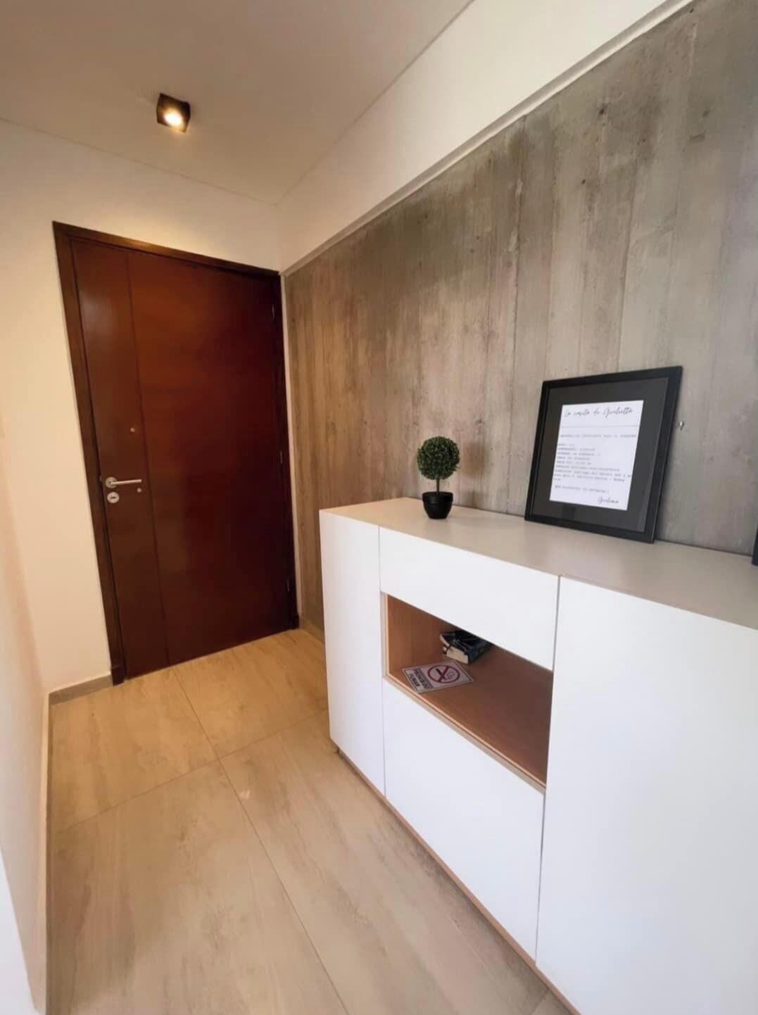 Um corredor com uma porta de madeira, um console branco com um certificado emoldurado e um pequeno vaso de planta.