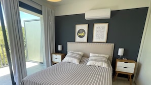 Un dormitorio moderno con una cama grande, dos mesitas de noche, una lámpara de techo y vistas al exterior.